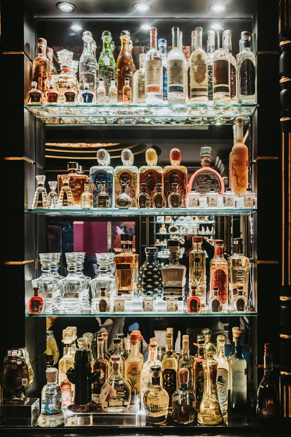 Botellas de tequila y mezcal expuestas en un estante de cristal de varios niveles.